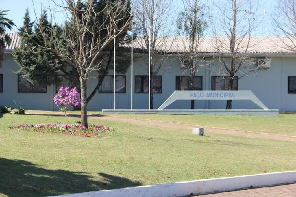Fachada do Paço Municipal de Reserva do Iguaçu, com árvores, jardim e canteiros em frente ao prédio público.