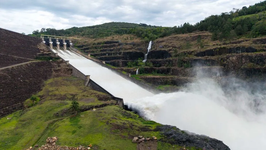 Vertedouro da Usina de Foz do Areia, em Pinhão, liberando grande volume de água, com formação de névoa entre encostas rochosas e vegetação, sob céu nublado.