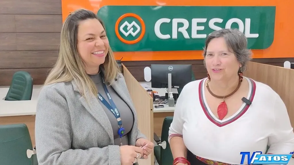 Danieli Mendes, à esquerda, e a jornalista Nara Coelho, à direita, na agência da Cresol em Pinhão, com a marca da cooperativa ao fundo e o logotipo da TV Fatos no canto inferior direito.