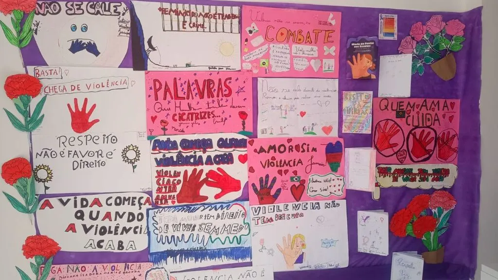 Painel com cartazes, desenhos e flores confeccionados por crianças, trazendo mensagens de combate à violência contra a mulher, respeito, proteção e valorização da vida.