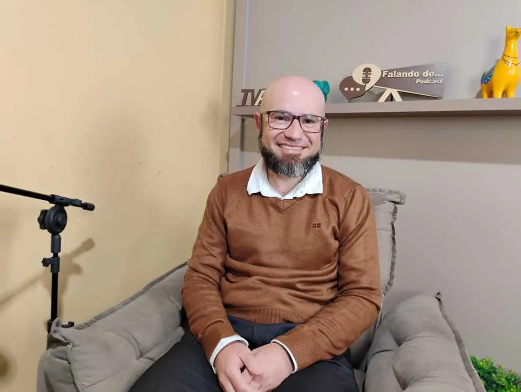 O psicólogo Ricardo Almeida, sorrindo e sentado em uma poltrona no estúdio do podcast Falando de..., da TV Fatos.