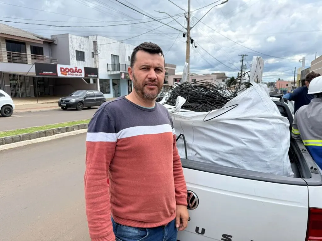 Vereador Edson Francesconi de Oliveira ao lado de uma caminhonete branca carregada com cabos, em uma rua de Pinhão. Ao fundo, aparecem postes e fiação aérea.